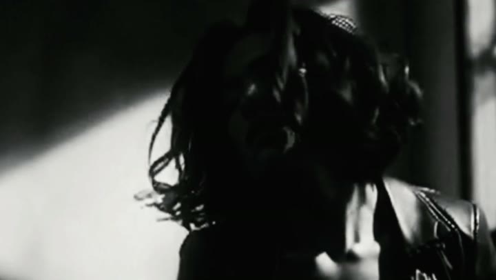 Black and white still from Un/Dress: a woman in motion, hair swinging through a shaft of hard light.